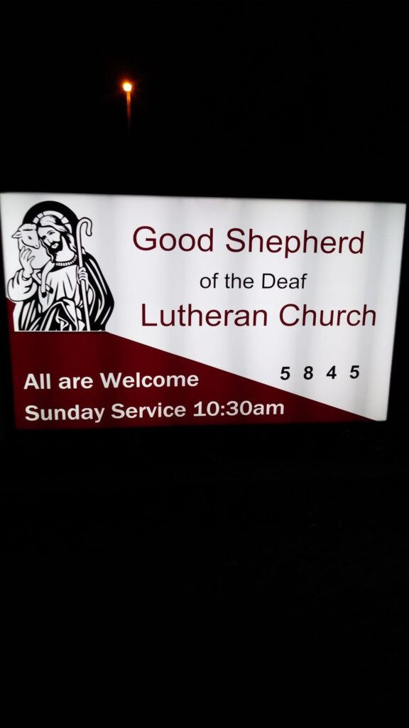 The front sign. Jesus carries a sheep and his crook. The sign is red and white with our name, Good Shepherd of the Deaf Lutheran Church.